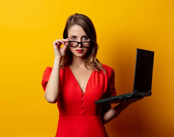 美しい女性で赤ドレスでラップトップコンピュータで黄色の背景 — ストック写真
