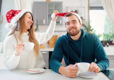 Noel şapkalı genç evli çift mutfakta kahve içiyor.