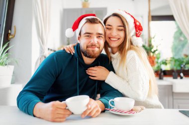 Noel şapkalı genç evli çift mutfakta kahve içiyor.