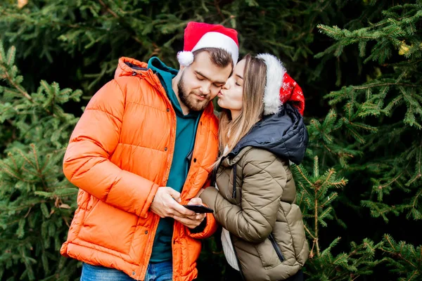 Girl kisses her boyfriend, and he is distracted by a mobile phon — Stock Photo, Image