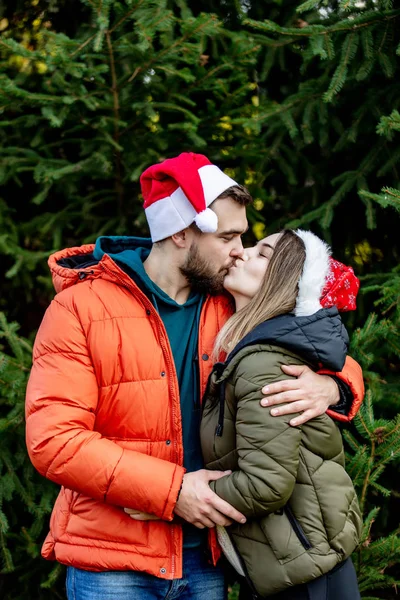 Romantic couple in Christmas hats near fir tree. — Stock Photo, Image