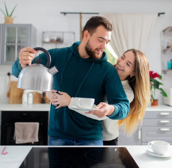 Junger Mann schüttet seiner Freundin kochendes Wasser aus einem Wasserkocher in — Stockfoto
