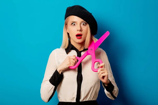 Beautiful french woman in beret big scissors on blue background — Stock Photo, Image
