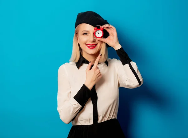 Hermosa mujer francesa en boina tiene despertador rojo en ba azul —  Fotos de Stock