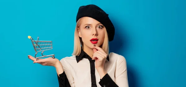 Schöne blonde Mädchen mit Warenkorb auf blauem Hintergrund — Stockfoto