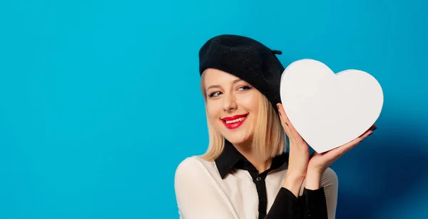 Beautiful Frenchwoman in a beret holds a heart-shaped box on a b — Stock Photo, Image