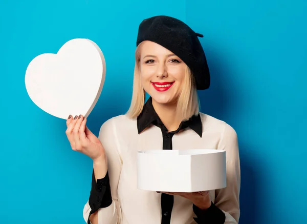 Beautiful Frenchwoman in a beret holds a heart-shaped box on a b — Stock Photo, Image
