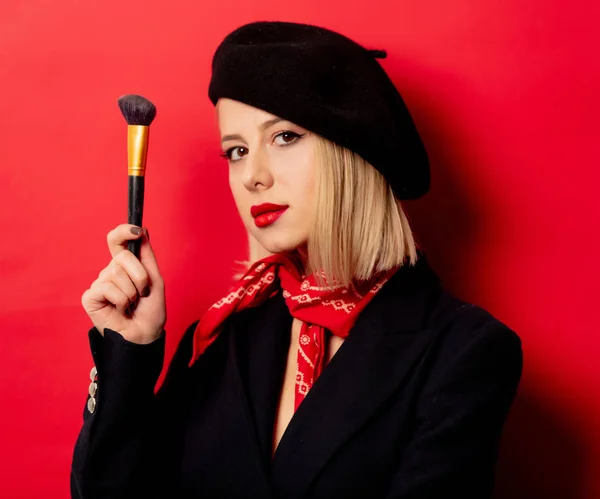 Hermosa mujer francesa en boina con cepillo de maquillaje sobre fondo rojo —  Fotos de Stock