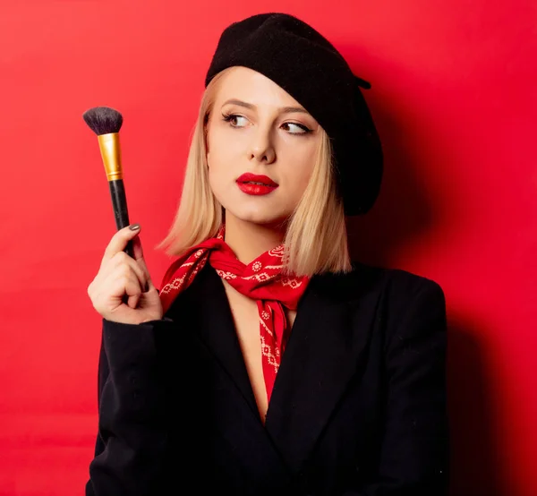 Hermosa mujer francesa en boina con cepillo de maquillaje sobre fondo rojo —  Fotos de Stock