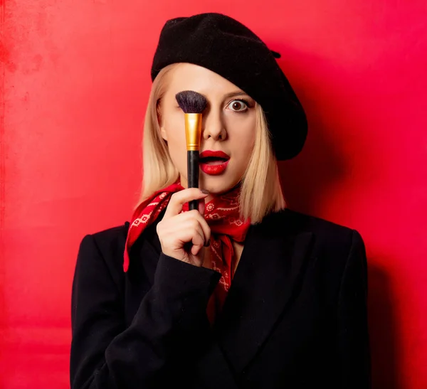 Beautiful french woman in beret with makeup brush on red backgro — Stock Photo, Image