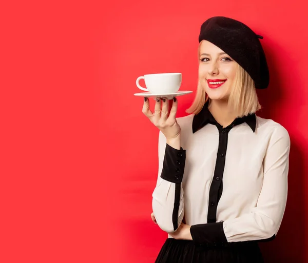 Hermosa mujer francesa en boina sostiene la taza de café en el respaldo rojo — Foto de Stock