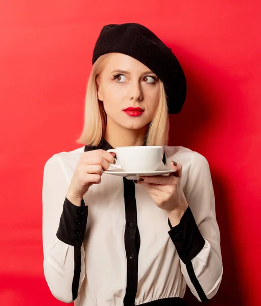 Schöne Französin in Baskenmütze hält Tasse Kaffee auf rotem Rücken — Stockfoto