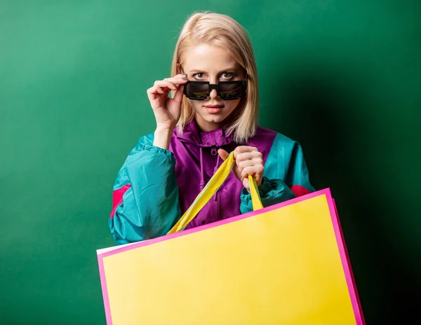 Szőke lány 90-es évekbeli stílusú kabát bevásárló táskák zöld hát — Stock Fotó