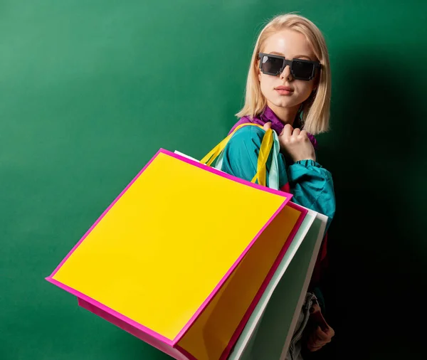 Blonde girl in 90s style jacket with shopping bags on green back — Stock Photo, Image