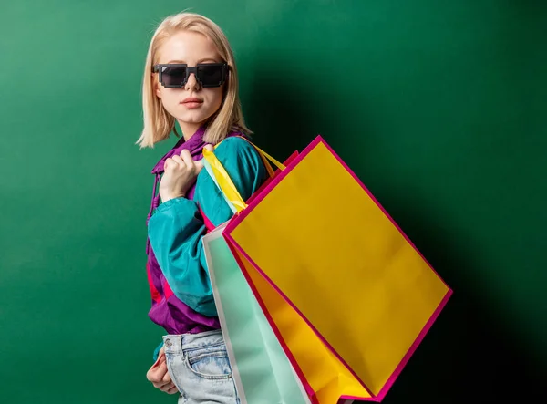 Menina loira nos anos 90 jaqueta de estilo com sacos de compras em verde de volta — Fotografia de Stock