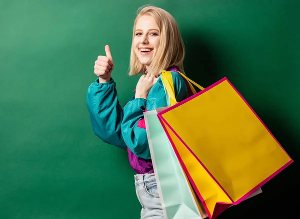 Blond tjej i 90-tals stil jacka med shoppingväskor på grön rygg — Stockfoto