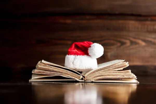 Παλιό βιβλίο και χριστουγεννιάτικο καπέλο σε ξύλινο τραπέζι — Φωτογραφία Αρχείου