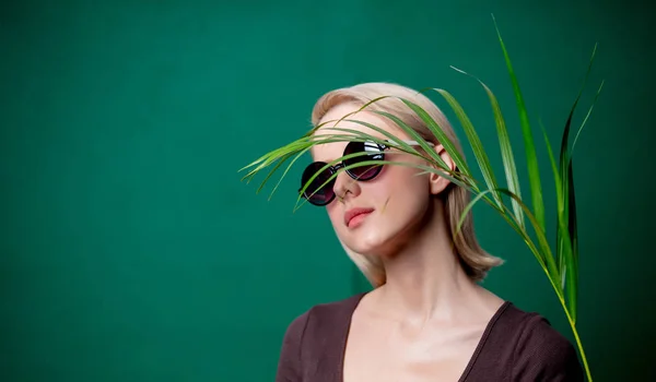 Woman in sunglasses with palm branch on green background — Stock Photo, Image