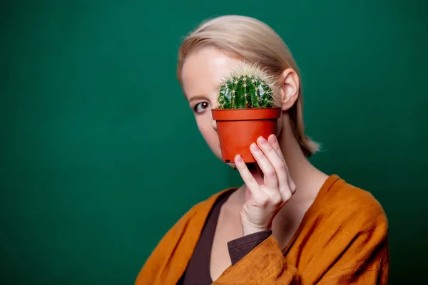 Woman holds cactus in her hand near a face on green background — ストック写真