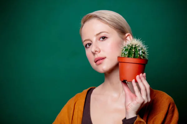 Женщина держит кактус в руке рядом с лицом на зеленом фоне — стоковое фото