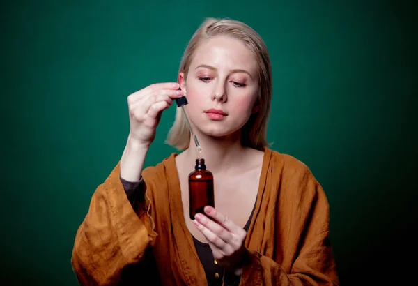 Mujer rubia con botella negra y pipeta sobre fondo verde — Foto de Stock