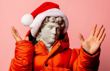 Ceket ve Noel Baba şapkası takmış antik bir heykel.