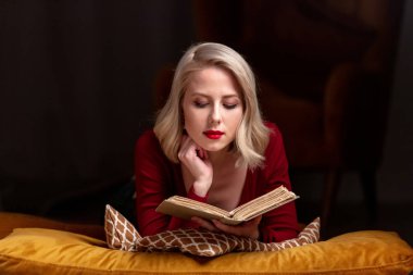 Kitaplı güzel sarışın kız yastıkların üzerinde yatıyor.