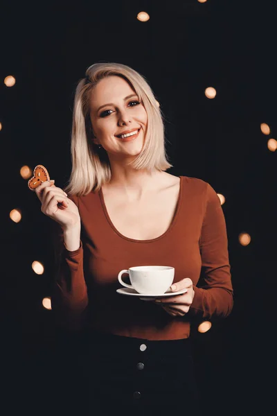 Blonde girl with cup of coffee and gingerbread cookie on backgro — 스톡 사진