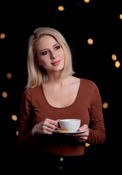 Blondes Mädchen mit Tasse Kaffee auf dem Hintergrund mit Lichterketten — Stockfoto