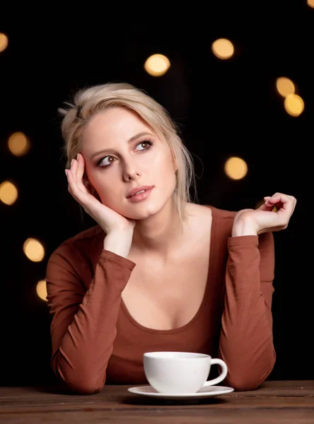 Menina loira com xícara de café no fundo com luzes de fadas — Fotografia de Stock