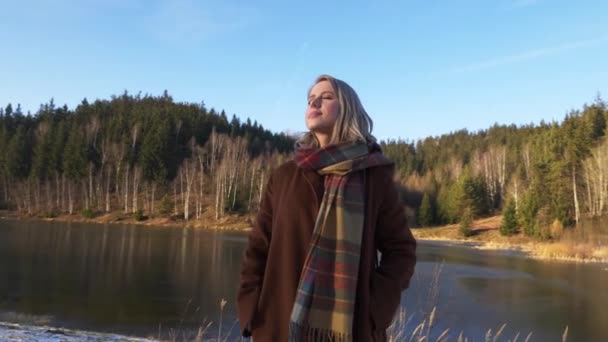 Ξανθιά Παλτό Και Μαντήλι Στέκεται Δίπλα Στη Λίμνη Στο Δάσος — Αρχείο Βίντεο