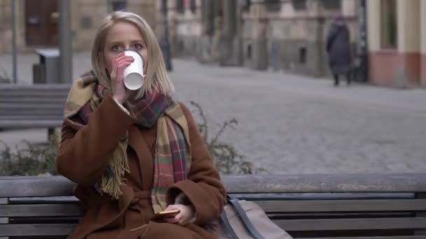 年轻女子喝了一杯咖啡 坐在街上的长椅上 — 图库视频影像