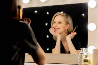 Makyaj aynasının yanında fırçası olan güzel sarışın kadın.