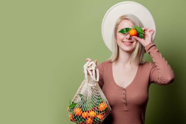 Young woman with mandarins in a string bag on green background clipart