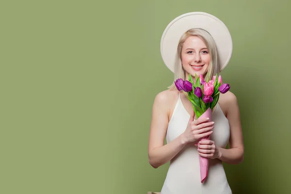 Schöne blonde Mädchen mit weißem Hut und Kleid mit Tulpen — Stockfoto