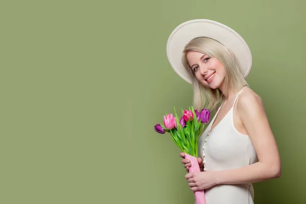 Vacker blond flicka i vit hatt och klänning med tulpaner — Stockfoto