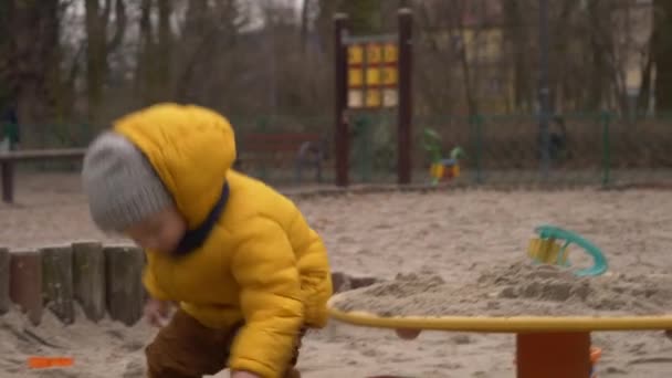 蹒跚学步的男孩在操场上的沙坑里玩耍 — 图库视频影像