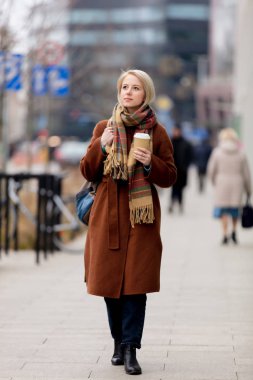 Şehir caddesinde elinde bir fincan kahve olan güzel sarışın kadın.