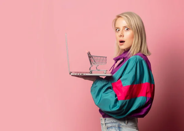Vrouw in de jaren 90 kleding met laptop computer en winkelwagen — Stockfoto