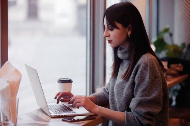 Laptop bilgisayarı olan esmer bir kadın kafede çalışıyor.