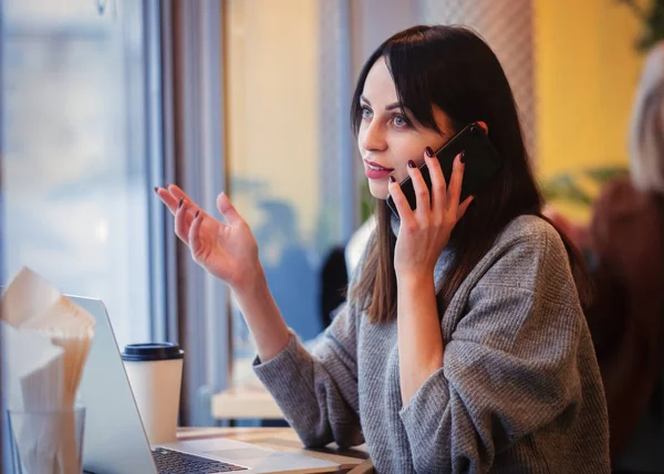 Donna con computer portatile e telefono cellulare che lavora in un caffè — Foto Stock