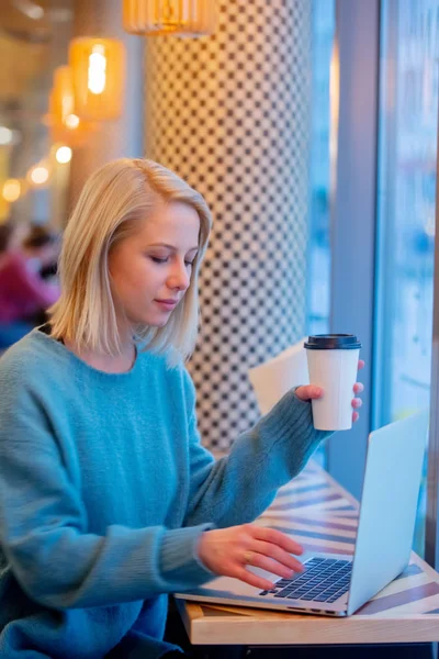Donna bionda bere caffè e lavorare con il computer portatile in un — Foto Stock