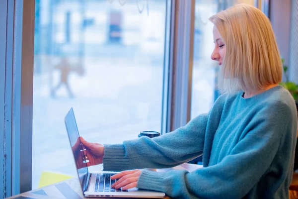 Donna bionda bere caffè e lavorare con il computer portatile in un — Foto Stock