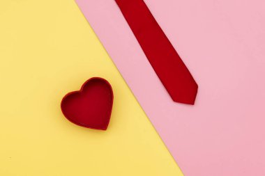 Kalp şeklinde hediye kutusu ve sarı ve pembe arka planda kravat.