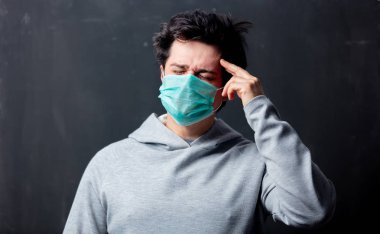 Baş ağrısı olan koruyucu maskeli genç beyaz bir adam.