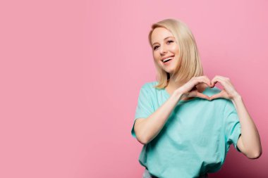 Güzel bir kadın pembe arka planda sevgi gösterisi yapar.