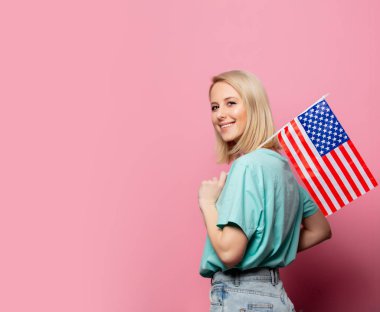 Pembe arka planda Usa bayrağı olan güzel sarışın kadın.