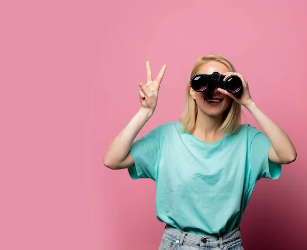 Mooie lachende vrouw met verrekijker op roze achtergrond — Stockfoto