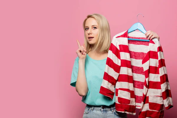 Mooie vrouw met shirt op een hanger op roze achtergrond — Stockfoto