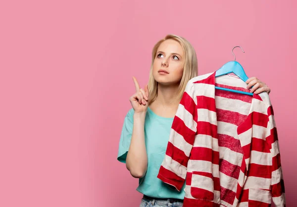 Mooie vrouw met shirt op een hanger op roze achtergrond — Stockfoto